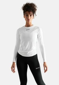 Hvid langærmet atletisk top med rund halsudskæring og subtile syninger, parret med sorte leggings med et logo. Glat tekstur.