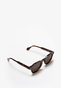 Braun gesprenkelte Sonnenbrille mit dunklen Gläsern, runder Form und dezent strukturiertem Rahmen. Metallakzente an den Bügeln.