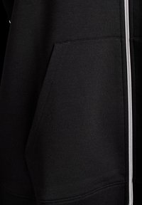 Černá mikina s kapucí a předním zipem a vnějšími kapsami, vyrobená z měkkého materiálu s hladkou texturou a zesílenými švy.