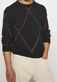 Černý pletený svetr s vícebarevným diagonálním prošíváním v červené, modré a žluté barvě. Žebrované manžety a výstřih s volným střihem.