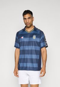 Maillot de football rayé bleu marine et bleu clair en matériau léger, avec un col, un logo et des accents sur les manches.