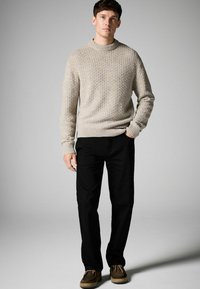 Beige textured knit sweater with a crew neckline, paired with black trousers and brown moccasin-style shoes. Simple, casual outfit.