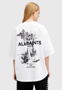 Camiseta blanca de gran tamaño con un gráfico negro de un ángel y elementos florales en la parte posterior, con el texto "ALLSAINTS LONDON".