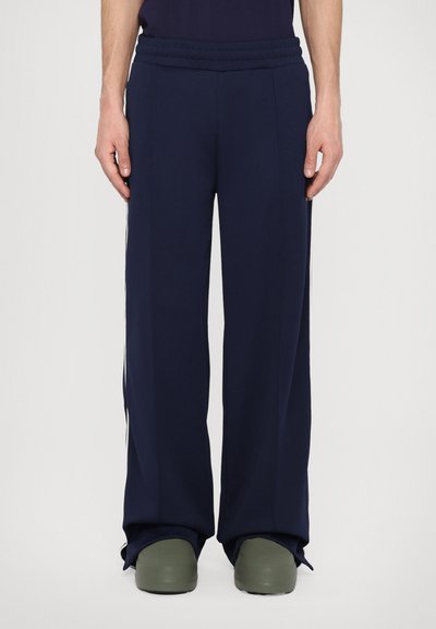 Pantaloni atletici de culoare albastru închis cu o croială lejeră, talie elastică și dungi laterale. Realizați dintr-un material neted și ușor.