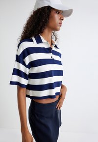 Marineblå og hvid stribet cropped polo skjorte med krave, korte ærmer og knapdetalje, parret med en marineblå nederdel. Tekstureret stof.