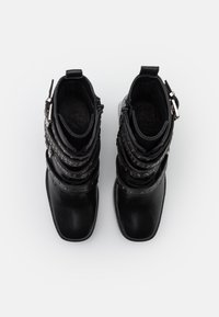 Botas de tobillo de cuero negro con correas superpuestas, detalles de tachuelas y punta redondeada. Presenta cremalleras dobles y un interior texturizado.