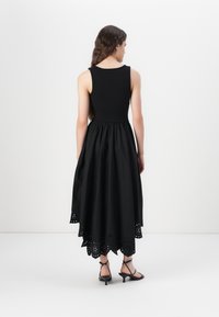 Black sleeveless dress featuring a fitted bodice and a flared skirt with a scalloped hem, decorated with cut-out detailing at the edges.