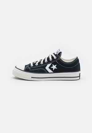 Black canvas sneakers with white accents, featuring a star logo, white laces, a rubber toe cap, and a textured white sole.