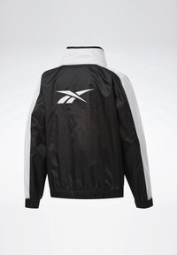 Coupe-vent noir et blanc avec poignets et ourlet élastiques, avec un grand logo blanc au centre du dos.