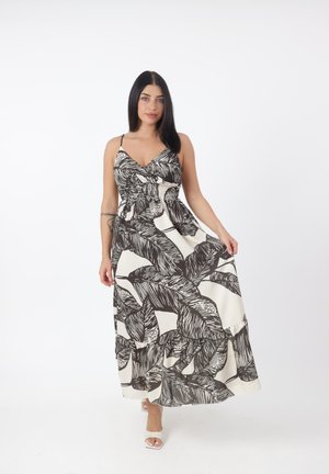 Donna con lunghi capelli scuri che indossa un vestito lungo senza maniche con motivi di foglie nere e bianche, che tiene la gonna e cammina in avanti.