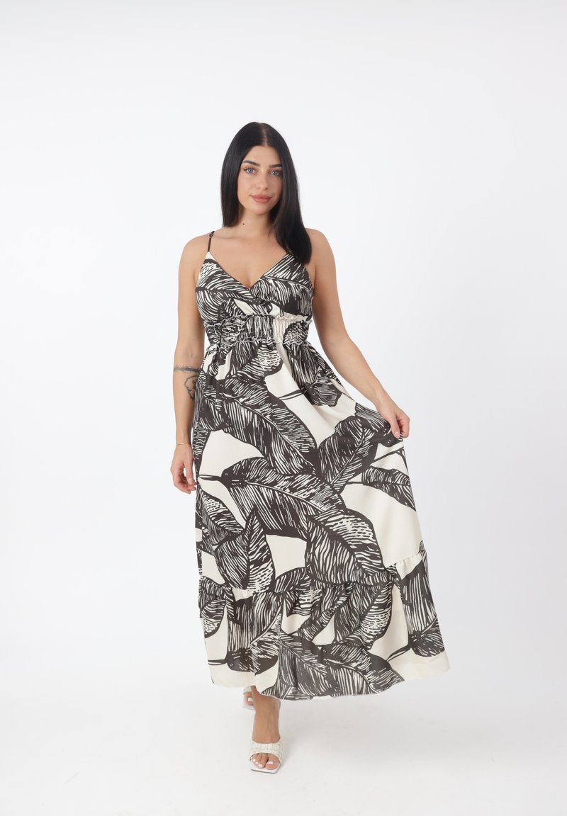 Mujer con cabello largo y oscuro que lleva un vestido maxi sin mangas con patrones de hojas en blanco y negro, sujetando la falda y caminando hacia adelante.