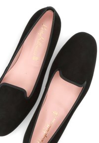 Schwarze Wildleder-Ballerinas mit runder Zehenpartie, rosa Innensohle und kontrastierendem schwarzen Rand entlang der Kanten. Goldenes Logo auf der Innenseite gedruckt.