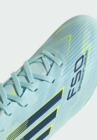Chaussure de football bleu clair avec lacets, rayures noires et jaunes, et texte "F50 Sparkfusion" sur une surface texturée.