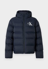 Marineblauwe pufferjack met capuchon, ritssluiting aan de voorkant, zijzakken en wit "cK" logo op de linkerkant van de borst.