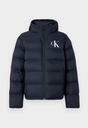 Marineblauwe pufferjack met capuchon, ritssluiting aan de voorkant, zijzakken en wit "cK" logo op de linkerkant van de borst.