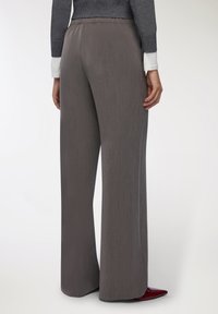Szare spodnie o szerokich nogawkach z teksturowanym wykończeniem, elastycznym pasem i subtelnymi pionowymi paskami, zestawione z bordowymi, spiczastymi butami.