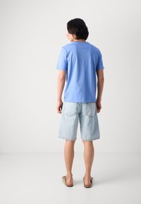 Lys blå bomullst-skjorte med korte ermer, kombinert med lysvaskede denimshorts, fullført med slip-on fottøy og avslappet passform.