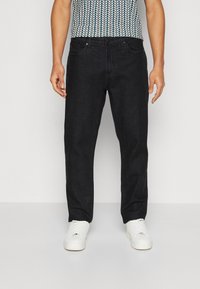 Jean en denim noir à coupe droite, avec cinq poches et des détails de couture subtils, assortis à des baskets blanches.
