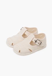 Beige canvas schoenen met een open teen ontwerp, klittenband en een gespsluiting. Vlakke rubberen zool en gestikte accenten op het bovenmateriaal.