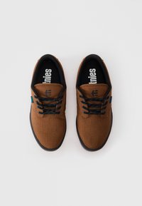 Paar pruunist kangast tenniset суп чорных подошвах и синих шнурках, вид с высоты на белом фоне.