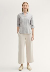 Camasa kaki deschis cu nasturi, dotată cu două buzunare pe piept, asortată cu pantaloni largi crema și pantofi cu platformă bej deschis. Material texturat.