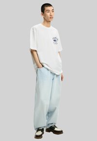 White short-sleeve t-shirt with "YUNG" graphic, paired with light blue wide-leg jeans, and black-and-white shoes. Simple, casual design.