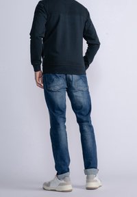 Ciemnogranatowy sweatshirt z teksturowanymi ramionami, w połączeniu z jasnoniebieskimi dżinsami i neutralnymi trampkami, z naciskiem na detale dotyczące fasonu i stylu.