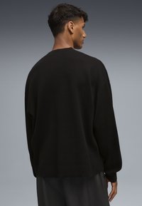 Maglione in lana nero oversize con scollo ampio, spalle abbassate e orlo a costine. Tessuto morbido senza motivi visibili.