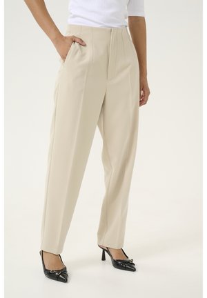 Beige tailored trousers with side pockets, straight leg design, and subtle front pleats, paired with black pointed toe heels.
