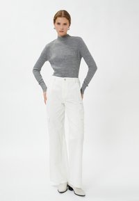 Maglione grigio a coste con collo alto, abbinato a pantaloni cargo bianchi a gamba larga con tasche laterali, mostrato con stivaletti crema alla caviglia.
