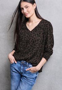 Hnědá bluzka s leopardím potiskem a výstřihem do V, zúženými rukávy, v kombinaci s modrými denimovými džínami. Hladká látka, volný střih.