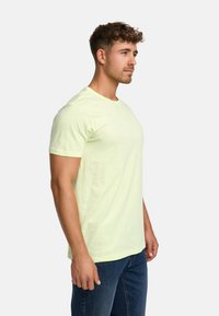 Light yellow cotton t-shirt with a crew neck, short sleeves, and a relaxed fit, worn with blue denim jeans. Minimalist design.
