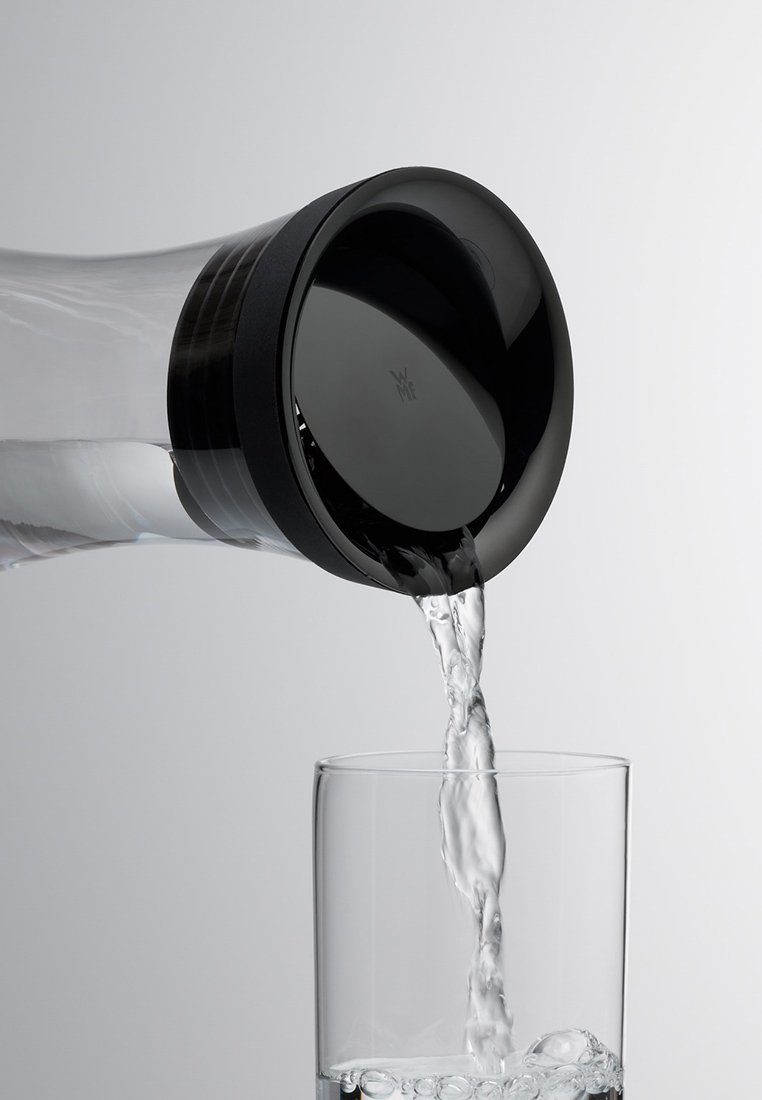 Przezroczysta szklana butelka na wodę z czarną plastikową nakrętką nalewająca wodę do przezroczystej szklanki. Gładki, zaokrąglony kształt, minimalistyczny styl.