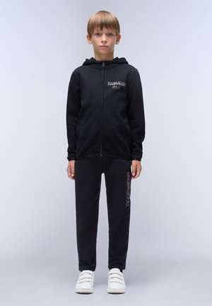 Zwarte zip-up hoodie met voorzak en logo detail, gecombineerd met zwarte sweatpants met tekst op de zijkant, gedragen met witte sneakers.