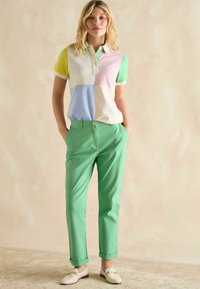 Pastelsetes toonides (kollane, roheline, roosa, sinine) kraega polosärk, mida on kombineeritud roheliste pükstega, millel on osaliselt üles rullitud mansett ja stiilne disain.