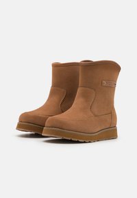 Botines de ante color caramelo con puntera redondeada, que cuentan con una costura decorativa, una pequeña etiqueta con el logo y una suela de goma resistente.