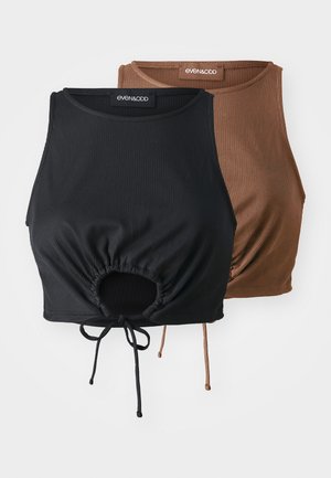 To ribbede crop tops i svart og brun, med snøringdetaljer og en samlet midje. Materialet ser mykt og elastisk ut.
