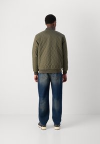 Veste bomber verte matelassée avec des poignets et un ourlet côtelés, associée à un jean ample bleu clair avec des poches arrière et des détails de décoloration.