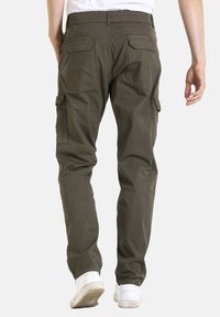Pantalons cargo vert olive en tissu léger, dotés de multiples poches, d'une coupe décontractée et de poignets élastiques. Portés avec des baskets blanches.