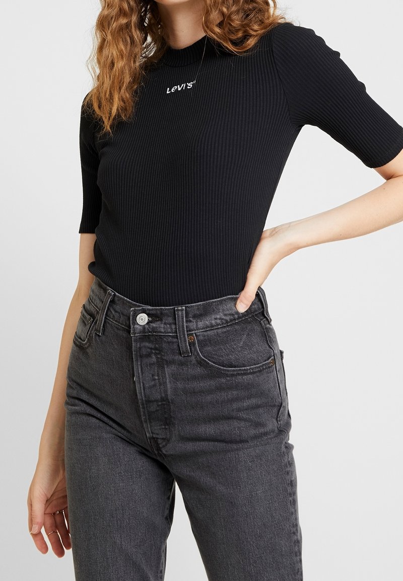 Top noir côtelé à manches courtes avec le logo Levi's, associé à un jean en denim gris taille haute, avec fermeture à bouton et à zip.