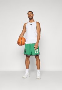 Balts bezpiedurkņu topiņš, zaļas acs basketbola šortus ar melnu apdari un numuru 19, turot basketbola bumbu, valkājot baltas sporta kurpes.