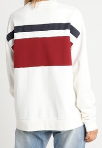 Felpa bianca con una sezione centrale rossa e strisce blu navy sulle spalle. Tessuto morbido con una vestibilità rilassata.