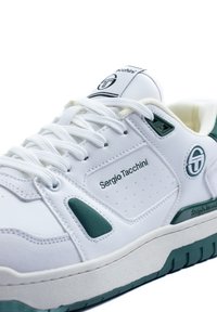 Bijela tenisica s zelenim detaljima, s glatkim kožnim gornjim dijelom, perforiranim detaljima, podstavljenim jezikom i debelim gumeni potplat.