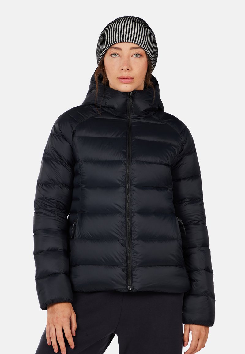 Giubbotto imbottito nero con cappuccio, caratterizzato da un design trapuntato, chiusura a zip e tasche laterali. Abbinato a un berretto a righe bianche e nere.