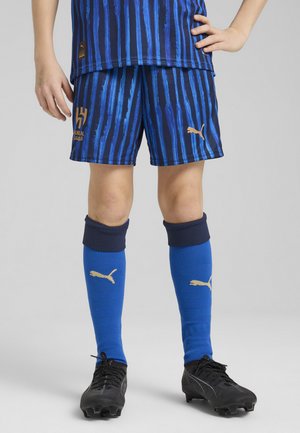 Ungdomsfotbollskit med blå och marinrandiga shorts, blå strumpor med guld Puma-logotyp och svarta fotbollsskor. Elastisk midja för komfort.