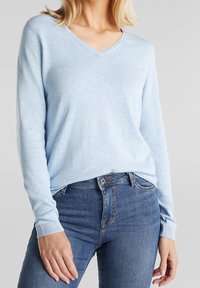 Vaaleansininen v-kaula-aukollinen neulepaita, valmistettu pehmeästä neuloksesta. Pitkät hihat ja resorit hihoissa, yhdistetty tummiin farkkuihin.