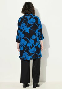 Wielokolorowa tunika z czarnym tłem, dużymi niebieskimi wzorami kwiatowymi, długimi rękawami i luźnym krojem, zestawiona z czarnymi spodniami o szerokich nogawkach.