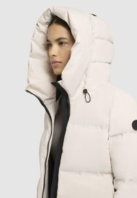 Puffy white down jacket featuring a large hood, black zipper, and black hardware accents. Smooth texture with quilted pattern detail.