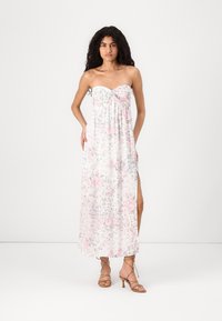 Maxi-dress ilman olkaimia kevyestä kankaasta, valkoinen vaaleanpunaisilla kukkakuoseilla, jossa on rypistetty rintaosa ja sivuhalkiot liikkumisen helpottamiseksi.