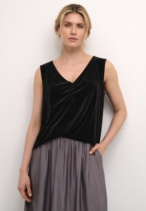 Top sans manches en velours noir avec un col en V et un détail froncé au centre, associé à une jupe grise fluide.